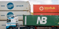 Halléns lastbil transporterar en grön NB-container framför staplade containrar från Schmidt och InterBulk Group