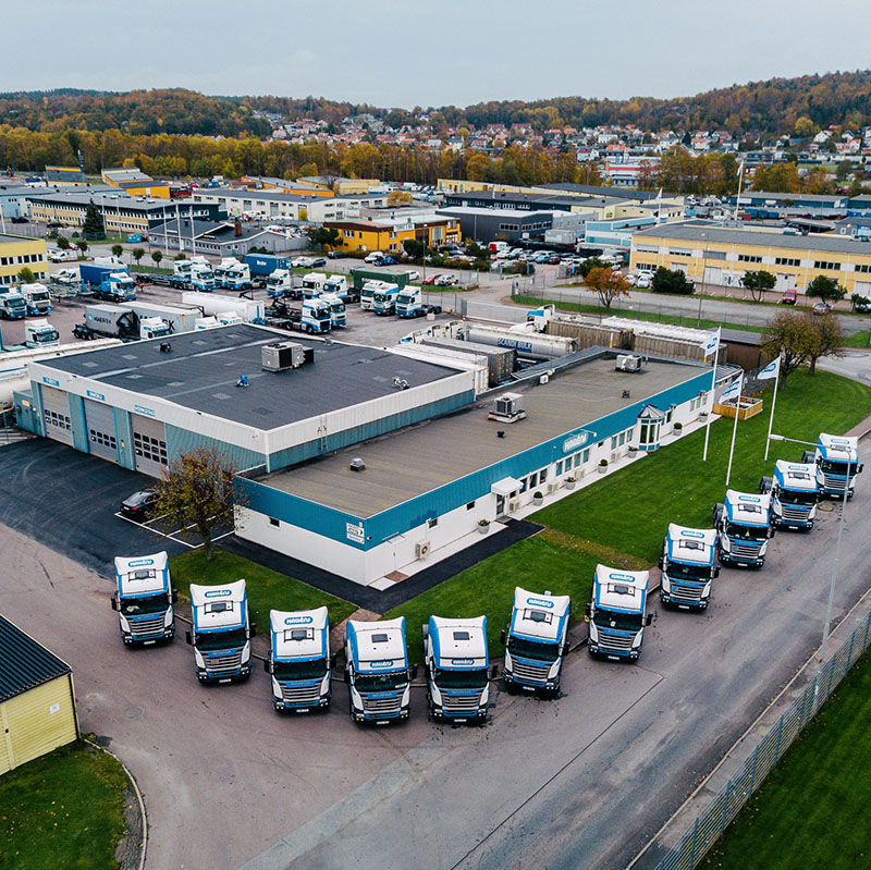 Flygbild över Halléns transportanläggning med lastbilar parkerade i formation framför byggnaden.